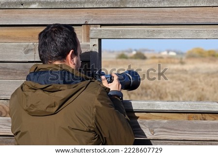 Wildlife photographer taking pictures at a bird reserve. Young caucasian man birdwatching in Laguna de la Nava, Valladolid, Spain.