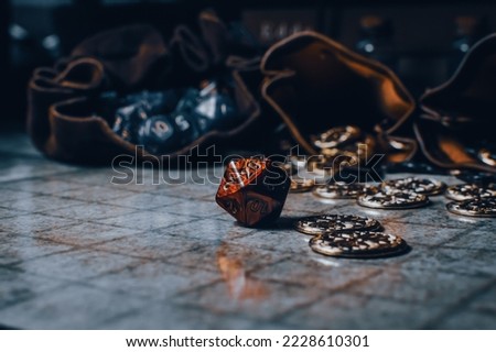A red role-playing gaming die on a gaming grid with game coins and dice bags Royalty-Free Stock Photo #2228610301