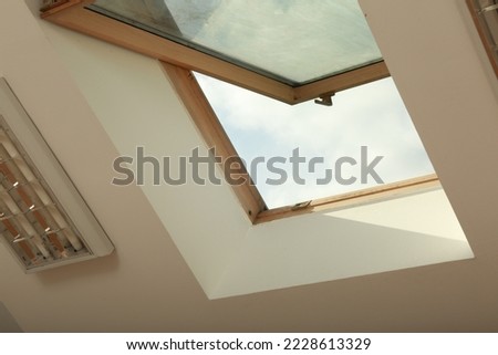 Open skylight roof window on slanted ceiling in attic room, low angle view Royalty-Free Stock Photo #2228613329