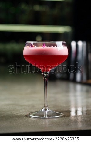Clover Club cocktail in coupe glass with layer of foam on dark background. Clover club alcoholic cocktail made from gin, raspberry syrup, egg white and lemon juice on the bar.