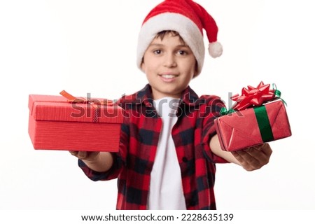 Selective focus on happy Christmas or New Year's gifts in hands of blurred pretten boy in Santa hat, smiling looking at camera, isolated on white background. Time to open presents. Winter holidays