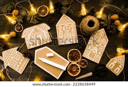 On a wooden background, a craft made of cardboard, a garland of paper houses on a jute rope next to oranges, cones, the atmosphere of the holiday Christmas and New Year.  Flat lay, decorative postcard