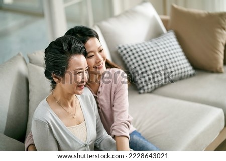 portrait of asian elderly mother and adult daughter sitting on couch at home happy and smiling