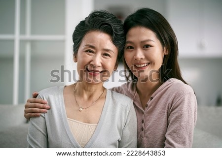 portrait of asian elderly mother and adult daughter sitting on couch at home happy and smiling