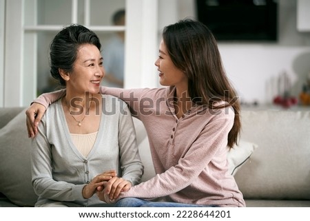 asian adult daughter and senior mother sitting on couch at home having a pleasant conversation Royalty-Free Stock Photo #2228644201