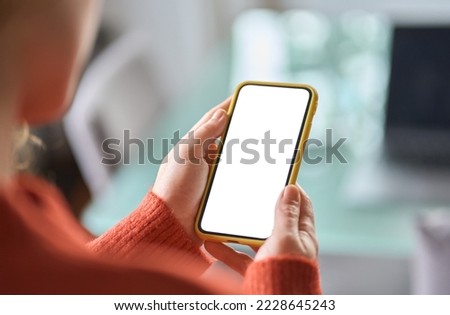 Over shoulder view of woman holding smartphone with white blank mock up cellular screen mobile applications using cell phone. Cellphone display mock up for advertising apps concept. Royalty-Free Stock Photo #2228645243