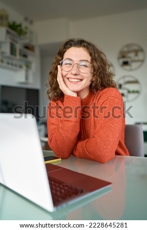 Young happy pretty business woman student sitting at desk at home office with laptop computer looking at camera advertising online learning, remote work, business webinars. Vertical portrait. Royalty-Free Stock Photo #2228645281
