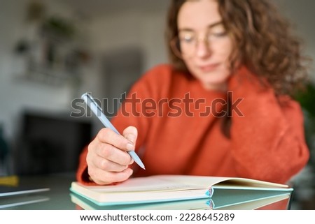 Business woman or young female student holding pen in hand writing in paper notebook journal, taking notes studying, doing homework, making checklist. Close up view Royalty-Free Stock Photo #2228645289