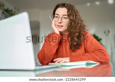 Young pretty woman student using laptop elearning or remote working at home office using laptop computer watching webinar, learning web course, studying online sitting at table, writing notes. Royalty-Free Stock Photo #2228645299