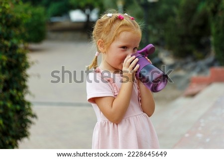 Little girl drinks sports bottled water in a city park