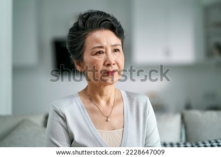 portrait of an unhappy senior asian woman sitting on couch at home Royalty-Free Stock Photo #2228647009