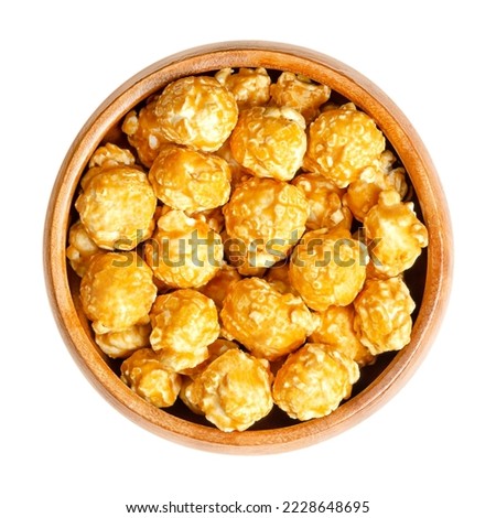 Caramel popcorn, caramel corn or also toffee popcorn, in a wooden bowl. Confection made of popped popcorn, with  a sugar or molasses based thin caramel candy shell. Sweet flavored, crunchy snack food.