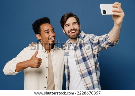 Young two friends men 20s wear white casual shirts together doing selfie shot on mobile cell phone post photo on social network isolated plain dark royal navy blue background. People lifestyle concept