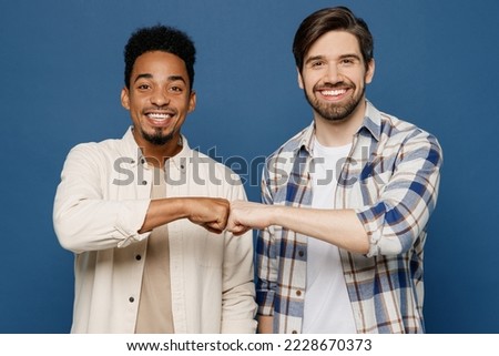 Young two friends cheerful cool smiling men 20s wear white casual shirts looking camera together give fistbump isolated plain dark royal navy blue background studio portrait. People lifestyle concept Royalty-Free Stock Photo #2228670373