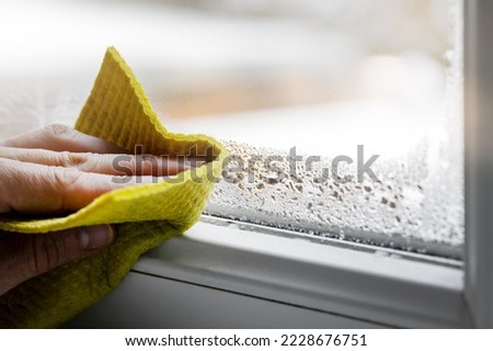 high humidity in the house. hand wipes off water condensation from plastic window glass in the room. home moisture Royalty-Free Stock Photo #2228676751