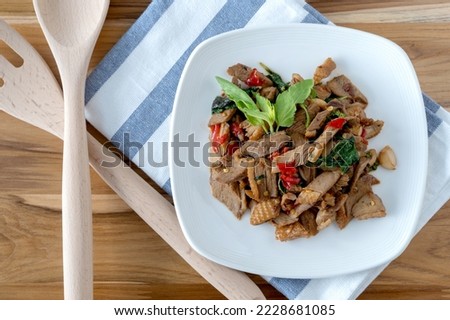 Stir Fried Duck with Holy Basil Beautiful pieces of duck meat, golden brown. Garlic and Basil Placed on a white plate on a cloth on a wooden table with chilli, garlic and basil leaves