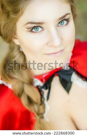 Portrait of a beautiful young woman in nature in the Little Red Riding Hood costume. Girl dressed as fairy-tale characters with beautiful make-up for Halloween