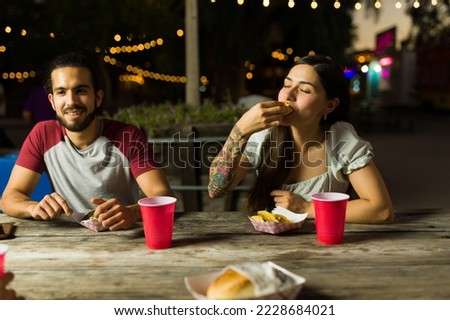 Hungry young woman and man eating delicious street tacos with friends at the food truck at night