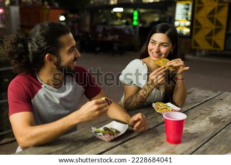 Smiling latin couple buying street food cart and eating delicious mexican food and tacos at night