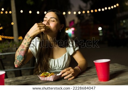 Attractive hispanic woman looking hungry enjoying eating delicious mexican tacos from the food truck at night