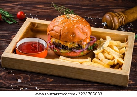Tasty burger cooking with beef, tomato, cheese, cucumber and lettuce. American cuisine beef burger with tomato, pickle, onion, lettuce, cheese sauce on a wooden board with french fries and ketchup. Royalty-Free Stock Photo #2228705033