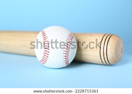 Wooden baseball bat and ball on light blue background, closeup. Sports equipment