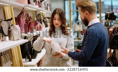 In a accessories store beautiful lady customer looking at the bags from the shelves while one charismatic salesman wants to help the customer