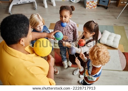 Above angle of little learners of nursery school and their teacher discussing characteristics of planets at lesson of astronomy Royalty-Free Stock Photo #2228717913
