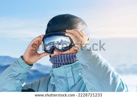 Close Up Of The Ski Goggles Of A Man With The Reflection Of Snowed Mountains. Man In The Background Blue Sky.  Winter Sports. Royalty-Free Stock Photo #2228721233