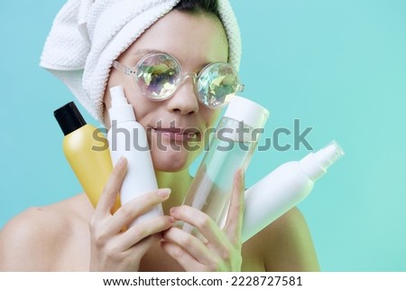 Horizontal photo, a woman with rare skin on a blue background in a towel in beautiful glasses with patches on her lips shows her best cosmetics