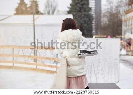 Woman looking to skating rink holding ice skates. Winter activities.