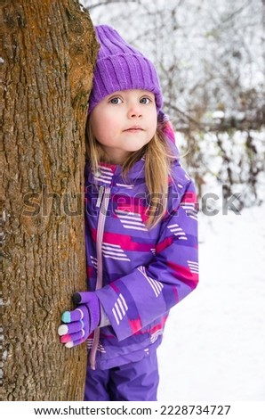 Beautiful little girl in purple jacket plays in a snowy winter park. Child playing with snow in winter.  Outdoors winter activities for kids.