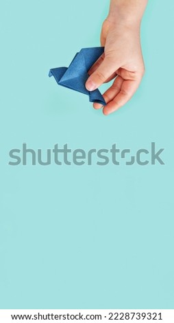 banner blue paper origami pigeon in children's fingers on blue background, copy space, vertical, 16:9