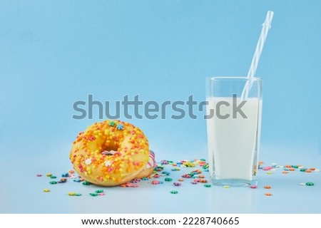 Donuts icing sprinkles with glass of milk on a pastel blue background. Doughnut and milk, breakfast concept.