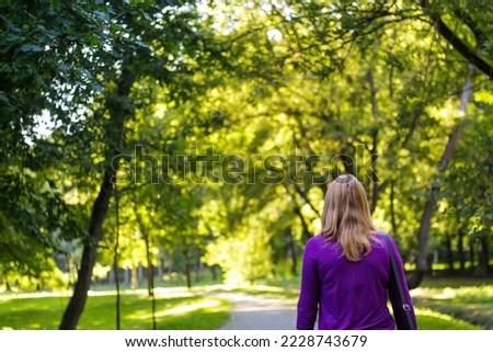 Defocus silhouette of a young woman looking at green park in the distance. Walking in the summer park. Copy space. Out of focus.