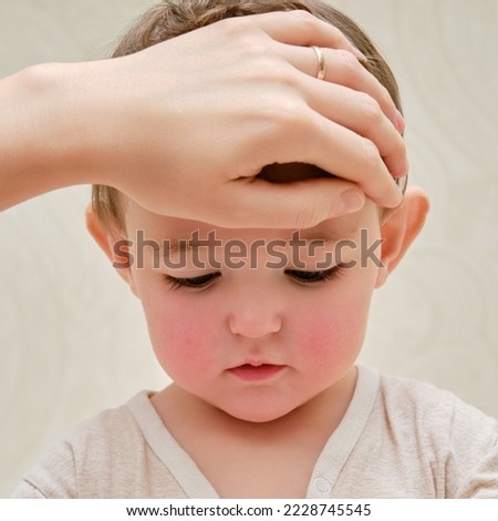 A mother woman measures the temperature of a ill toddler baby with her hand. Mom checks the high temperature of a sick child. Kid aged one year and three months Royalty-Free Stock Photo #2228745545