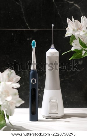 dental health care products, sensitive teeth brush and electric irrigator for daily individual usage and lilies flowers on dark marble background
