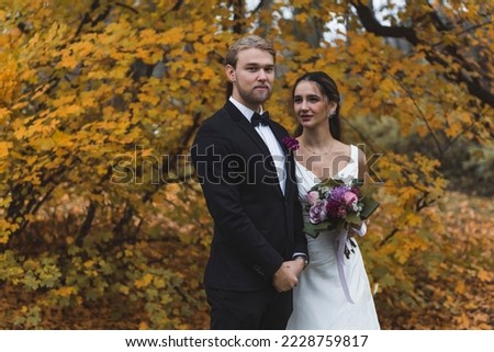 Amazing colors of autumn forest. Heterosexual couple during wedding photoshoot. Medium long shot of caucasian spouse and his Turkish wife standing next to each other in marital clothes. High quality
