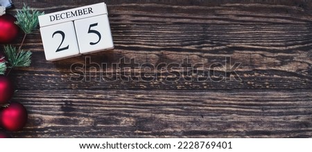 Web banner of wooden calendar blocks with the date December 25th to mark Christmas Day with holiday trim of red ornaments and pine tree branch. Top view with copy space available.