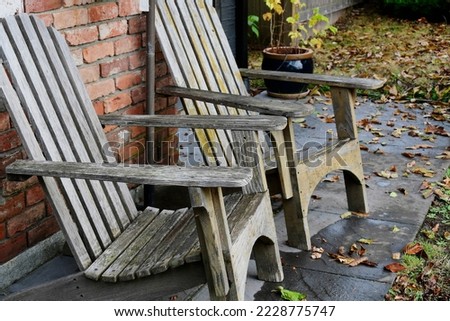 An image of two old and weathered deck chairs on a small stone patio in autumn. 