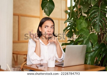 Young businesswoman thinking, frowning as sitting puzzled and complicated, using laptop in cafe.