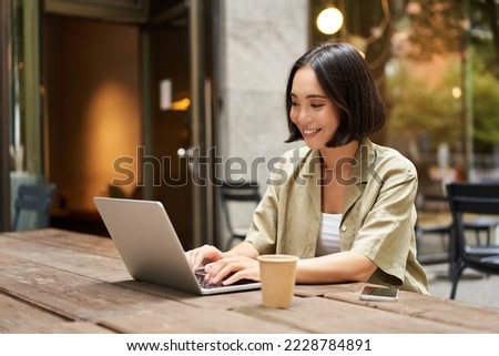 Young asian woman, digital nomad working remotely from a cafe, drinking coffee and using laptop, smiling. Royalty-Free Stock Photo #2228784891