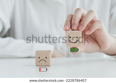 Hand holding happy smile face with full battery and unhappy face low battery on floor. Full energy, Passion, Happy Life, Emotion, positive thinking, world mental health day, mental health assessment. Royalty-Free Stock Photo #2228786407