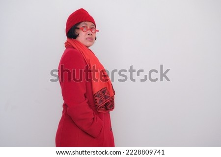 Side view: A middle-aged woman in red coat wearing glasses, red beanie and shawl.