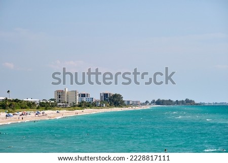 Resort beach with white sand, blue water, tall hotel buildings. Happy people sunbathing and swimming in ocean