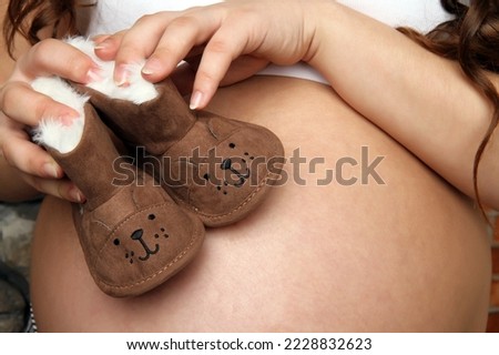 Pregnant tummy with brown baby shoes. The woman's hands are holding small funny shoes.