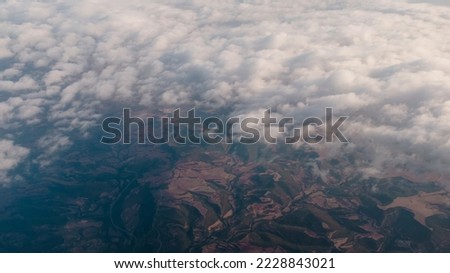 Cloudscape seen from the sky seeing through some brown agricultural fields, view from an airplane window Royalty-Free Stock Photo #2228843021