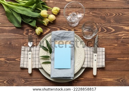 Stylish table setting with blank card and tulips on wooden background