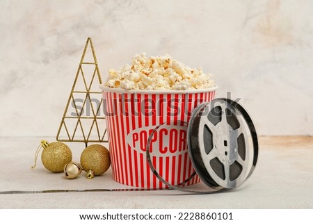 Bucket of popcorn with film reel and Christmas decor on light background