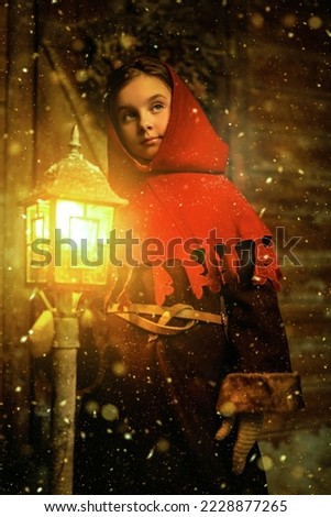 Once upon a Christmas. A cute little girl in medieval clothes stands by a wooden house and burning lantern on a snowy night. Christmas fairy tale.